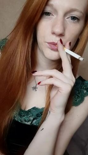 A red-haired women with long hair smokes a cigarette with a brown